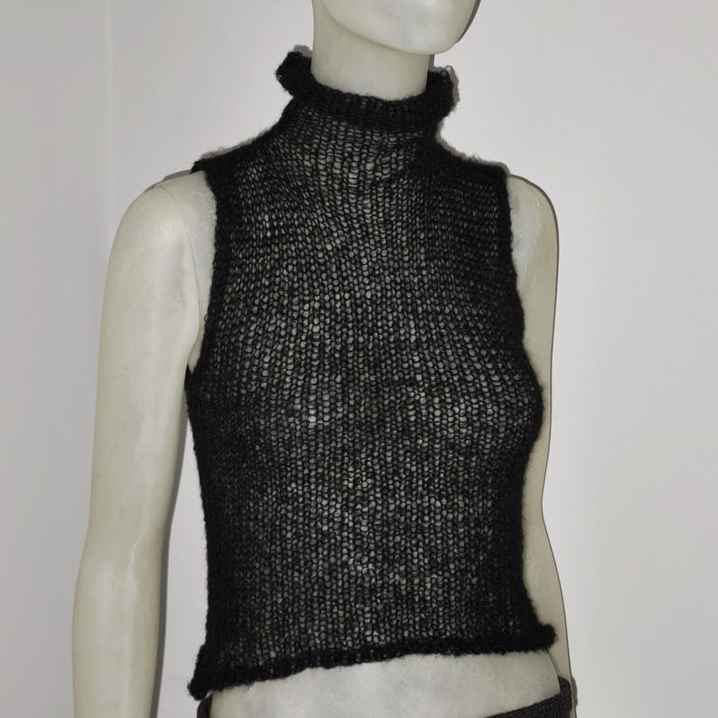 Op de afbeelding: Zwarte mouwloze coltrui. De top is gemaakt van los gebreid materiaal, met een hoge, gerimpelde halslijn en een licht verkorte zoom. Het kledingstuk wordt op een mannequin getoond.
