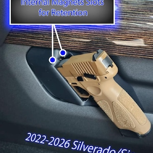 May include: Tan handgun with textured grip, placed in a vehicle's interior. Text reads "Internal Magnets Slots for Retention" and "2022-2026 Silverado/Sierra". The image highlights the gun's placement and retention system.