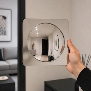May include: A square-shaped mirror with a circular convex center. The reflective surface is silver and smooth, featuring rounded corners. The circular center creates a wide-angle, distorted reflection of an interior room with white walls and dark doors.
