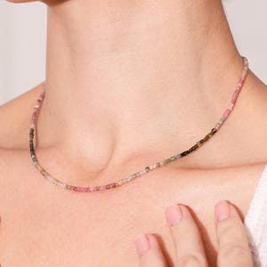 Puede incluir: Un delicado collar hecho de pequeñas cuentas multicolores. Las cuentas son una mezcla de rosa, verde y negro, creando un sutil efecto degradado. El collar es simple y elegante, perfecto para el uso diario.