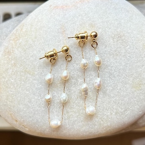 Puede incluir: Un par de pendientes de oro con una cadena de perlas blancas. Los pendientes tienen un diseño sencillo y son perfectos para el uso diario.