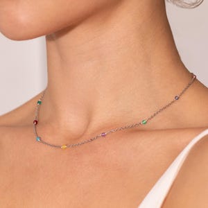 May include: A silver chain necklace with small colourful gemstones. The necklace features a variety of colours, including red, green, blue, purple, and yellow.