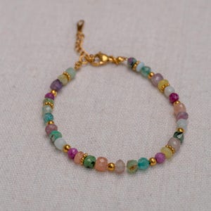 May include: A delicate bracelet with a gold chain and colorful gemstone beads. The beads are a mix of pink, green, blue, and yellow.
