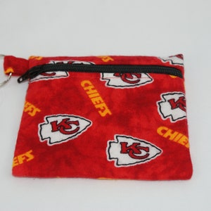 May include: A small, red fabric coin purse with a black zipper and a silver key ring. The purse is patterned with white and yellow logos and the word "CHIEFS".