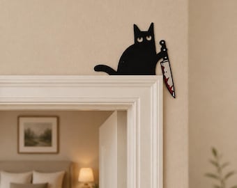 May include: A black cat wall decoration featuring a flat silhouette design. The cat is depicted with wide white eyes and is holding a large kitchen knife with red blood-like stains on the blade. The piece is positioned on the corner of a door frame.
