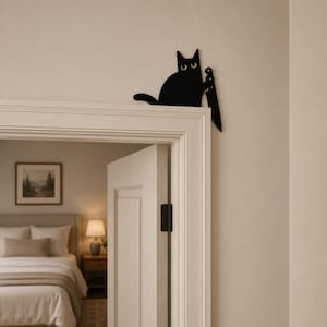 May include: A black metal wall decoration shaped like a cat holding a large knife, designed to be mounted on the corner of a door frame. The cat has wide white eyes and is positioned as if peering over the edge of the door frame trim.