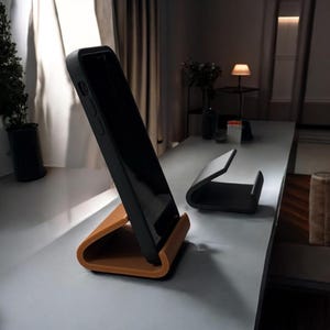 May include: A black phone case with a brown phone stand. The phone stand is on a white surface.