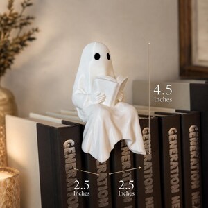 Puede incluir: Una figura de fantasma de cer&aacute;mica blanca, de 11,4 cm de altura, leyendo un libro mientras est&aacute; sentado sobre una pila de libros. Los libros miden 6,4 cm de ancho y tienen la palabra "GENERATION" impresa en el lomo. El fantasma tiene ojos negros.