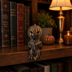 Small and large Halloween reading pumpkin shelf sitter figurines with antique bronze and gold finishes, displayed on a modern mantel. Decorative bookshelf accents for book lovers, cozy fall home decor, autumn displays, and spooky Halloween decoration.