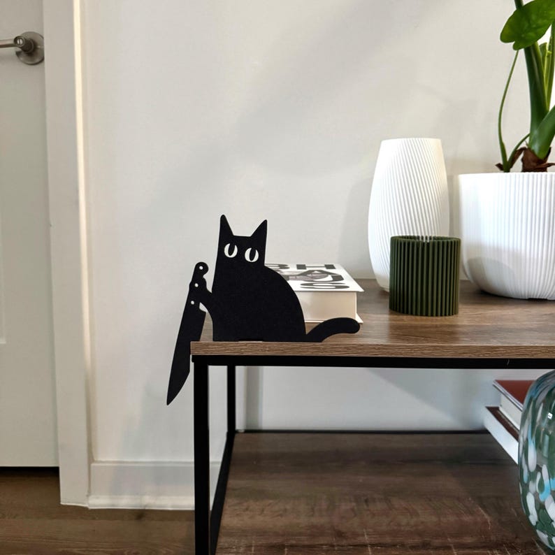 Black cat light switch cover topper with spooky knife design, perched above a triple light switch in a modern neutral home. Minimalist Halloween wall decor featuring a playful black cat silhouette. Perfect for kitchens, hallways, bathrooms, bedrooms, entryways, or any room, adding a unique gothic touch while fitting standard switch plates.