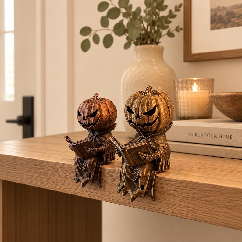 Small and large Halloween reading pumpkin shelf sitter figurines with antique bronze and gold finishes, displayed on a modern mantel. Decorative bookshelf accents for book lovers, cozy fall home decor, autumn displays, and spooky Halloween decoration.