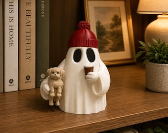 May include: A white ghost figurine wearing a red knit-style beanie with a pom-pom. The ghost has black oval eyes, holds a small brown coffee cup in one hand, and carries a small tan puppy in the other hand. The figure is smooth and matte.