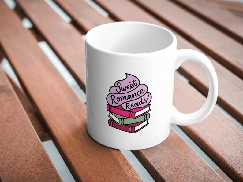 May include: White ceramic mug featuring a stack of books with the words "Sweet Romance Reads" in a whimsical font. The mug has a curved handle and is set against a wooden surface.