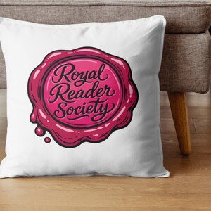 May include: White throw pillow featuring a pink and red wax seal design with the words "Royal Reader Society" in a cursive font. The pillow is on a wooden floor next to a gray couch.
