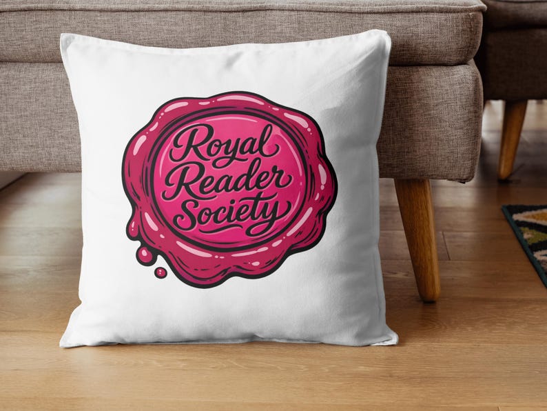 May include: White throw pillow featuring a pink and red wax seal design with the words "Royal Reader Society" in a cursive font. The pillow is on a wooden floor next to a gray couch.