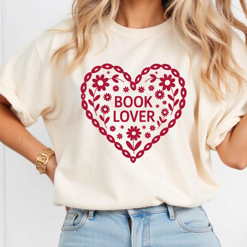 Puede incluir: Camiseta color crema con un dise&ntilde;o en forma de coraz&oacute;n burdeos. El coraz&oacute;n est&aacute; lleno de flores y las palabras "BOOK LOVER". La camiseta tiene mangas cortas y un corte holgado.
