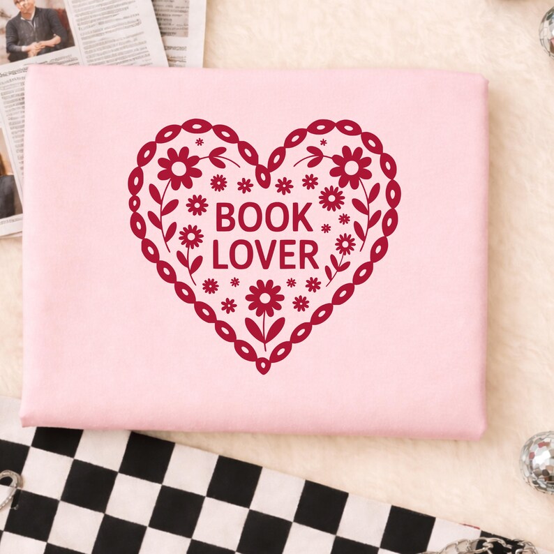 Puede incluir: Una portada de libro rosa claro con un dise&ntilde;o en forma de coraz&oacute;n burdeos. El coraz&oacute;n est&aacute; lleno de flores y hojas, y las palabras "BOOK LOVER" est&aacute;n en el centro. El dise&ntilde;o est&aacute; rodeado por un borde decorativo.