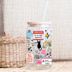 May include: A clear glass tumbler with a bamboo lid and a clear straw, featuring various colorful stickers including a sloth, a black cat, a fax machine, and text that reads "HELLO I'm an adult. Apparently." and "Bad vibes don't go with my lipstick."