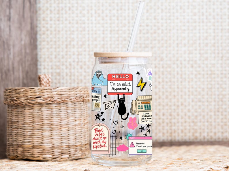 May include: A clear glass tumbler with a bamboo lid and a clear straw, featuring various colorful stickers including a sloth, a black cat, a fax machine, and text that reads "HELLO I'm an adult. Apparently." and "Bad vibes don't go with my lipstick."
