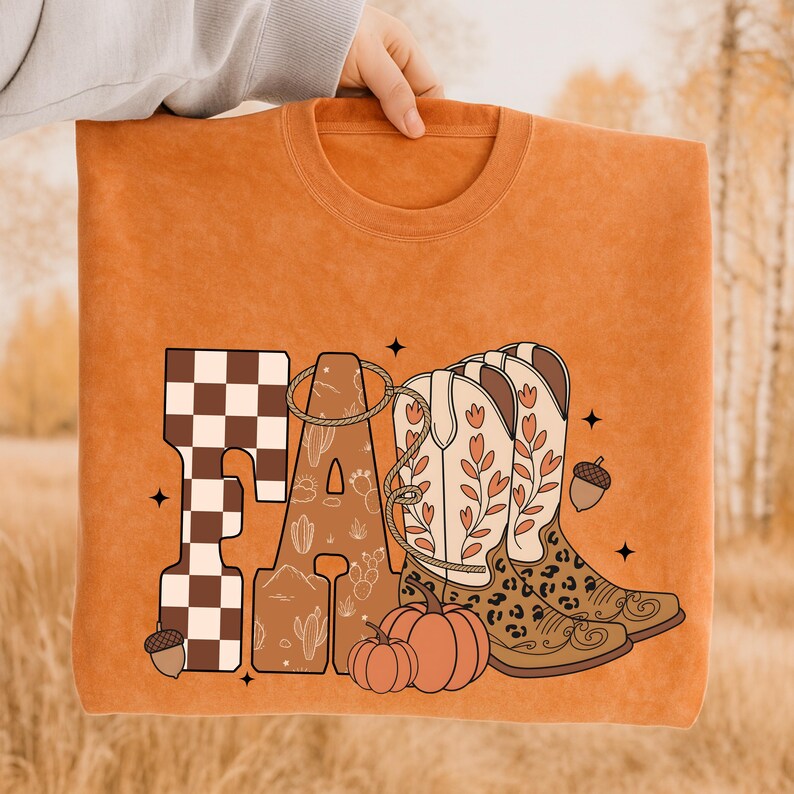May include: An orange crewneck sweatshirt featuring the word FALL in large letters. The F has a brown and white checkerboard pattern, the A contains cactus line art, and the LL are replaced by two cowboy boots with floral and leopard print.