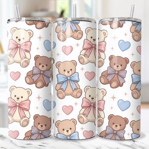 May include: A white tumbler with a repeating pattern of teddy bears, hearts, and stars. The teddy bears are in shades of brown and cream, each wearing a bow in pink or blue. The tumbler has a silver straw.