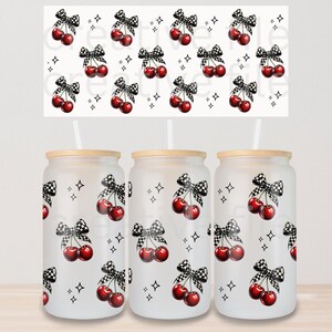 Peut inclure: Trois gobelets en verre d&eacute;poli avec couvercles en bois et pailles. Chaque gobelet pr&eacute;sente un motif r&eacute;p&eacute;t&eacute; de cerises rouges avec des n&oelig;uds &agrave; carreaux noirs et blancs et de petites &eacute;toiles noires. Un motif assorti est au-dessus des gobelets.