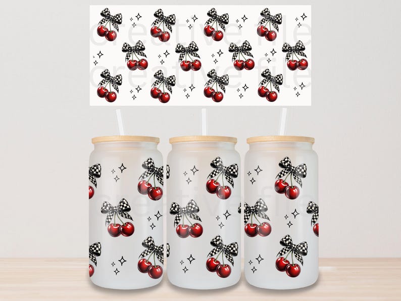 Peut inclure: Trois gobelets en verre d&eacute;poli avec couvercles en bois et pailles. Chaque gobelet pr&eacute;sente un motif r&eacute;p&eacute;t&eacute; de cerises rouges avec des n&oelig;uds &agrave; carreaux noirs et blancs et de petites &eacute;toiles noires. Un motif assorti est au-dessus des gobelets.