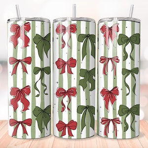 May include: Three stainless steel tumblers with a white background and green vertical stripes. Each tumbler is decorated with red and green bows. The tumblers have a straw and are on a wooden surface.