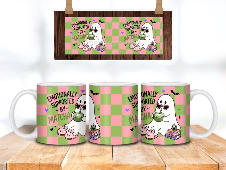 May include: A white ceramic mug featuring a pink and green checkered pattern with a cartoon ghost wearing heart-shaped sunglasses, drinking matcha, and sitting on books. The text reads EMOTIONALLY SUPPORTED BY MATCHA, with small hearts, bats, and slippers.