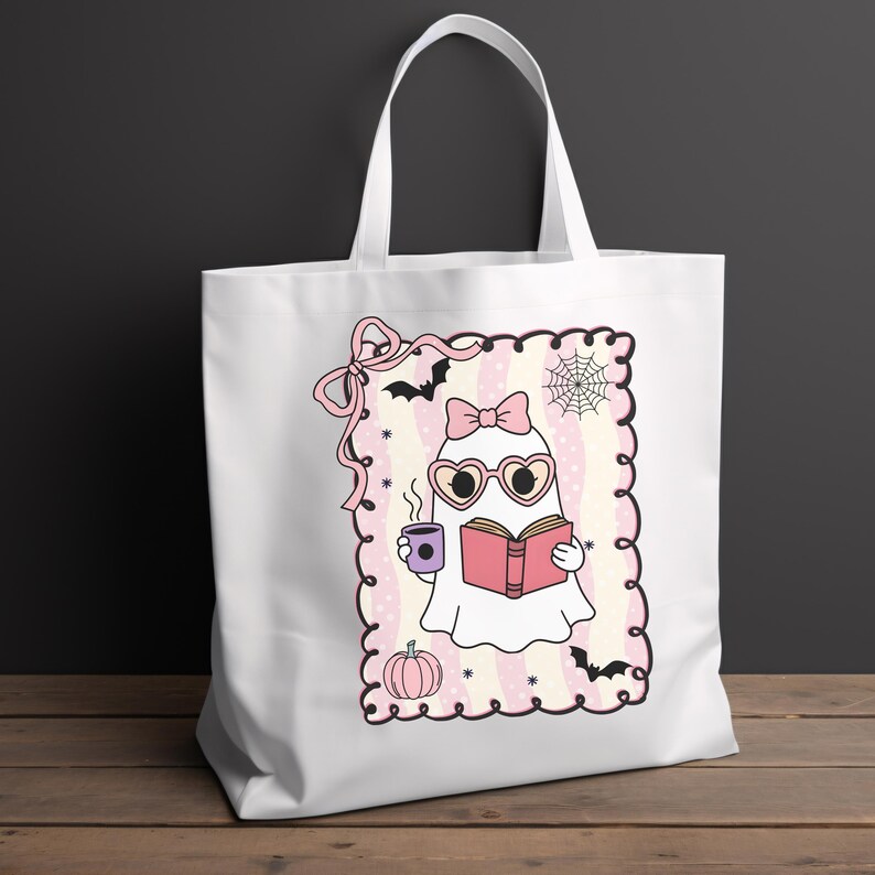 May include: White tote bag featuring a cartoon ghost reading a book and holding a coffee cup. The ghost wears heart-shaped glasses and a bow. The design includes bats, a spiderweb, and a pumpkin, all in pink and purple.