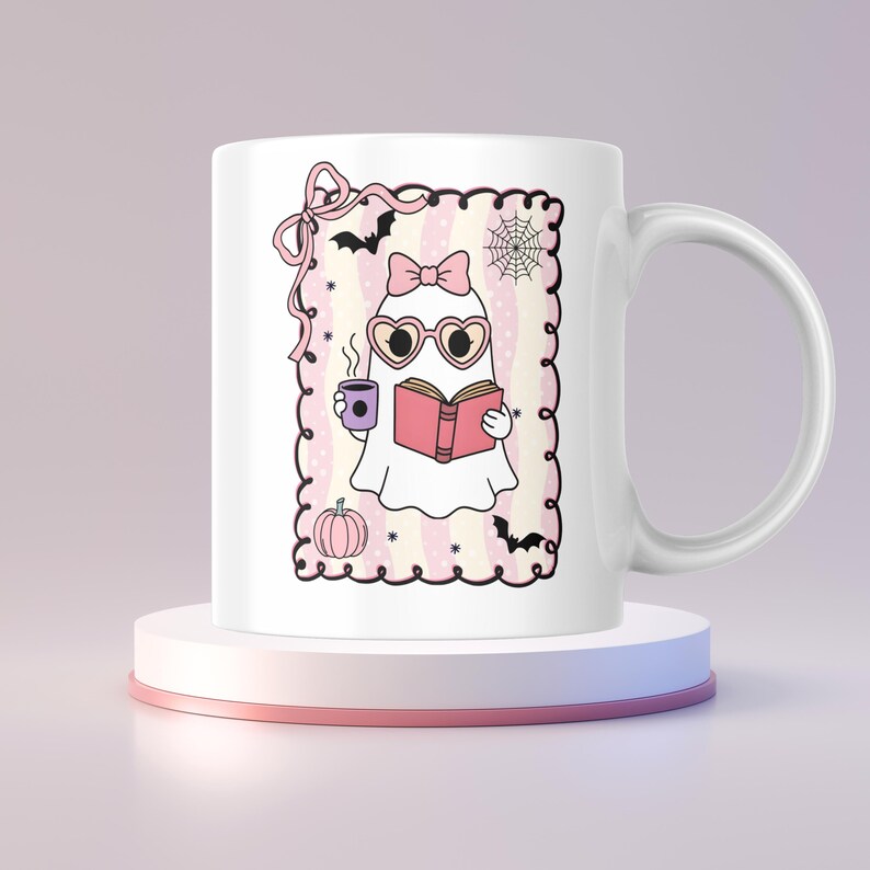 May include: White ceramic mug featuring a cartoon ghost reading a book and holding a cup. The ghost wears heart-shaped sunglasses and a pink bow. The design includes bats, a spiderweb, and a pumpkin, all within a pink and white striped frame.