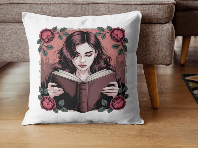 Puede incluir: Coj&iacute;n cuadrado blanco con una ilustraci&oacute;n de una mujer leyendo un libro, enmarcada por rosas rosas y hojas verdes. La mujer tiene cabello oscuro y ondulado y viste una blusa oscura. El fondo es de color rosa p&aacute;lido.