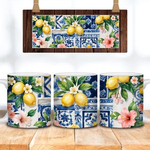 May include: Three white ceramic mugs with a watercolor design of lemons, flowers, and blue and white tile patterns. A matching rectangular sign hangs above the mugs. The mugs are on a wooden surface.