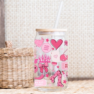 May include: A clear glass can-shaped tumbler with a bamboo lid and a straw. The tumbler is decorated with pink graphics including hearts, flames, and boots. The text "cute cute cute" and "NO BAD VIBES" are also visible.