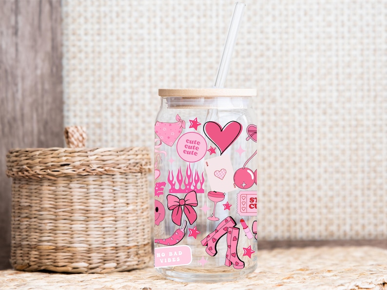 May include: A clear glass can-shaped tumbler with a bamboo lid and a straw. The tumbler is decorated with pink graphics including hearts, flames, and boots. The text "cute cute cute" and "NO BAD VIBES" are also visible.