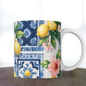 May include: White ceramic mug featuring a vibrant design of lemons, pink flowers, and green leaves against a backdrop of blue and white tiles. The mug has a curved handle and is suitable for hot or cold beverages.