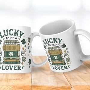 May include: Two white ceramic mugs with the text "LUCKY TO BE A BOOK LOVER" and a stack of books with shamrock and floral designs. The mugs are on a wooden surface.