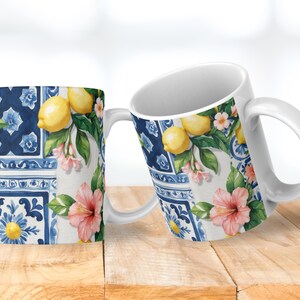 May include: Two white ceramic mugs with a vibrant design featuring lemons, pink flowers, and blue tile patterns. The mugs have a classic handle and are set against a wooden surface, showcasing a bright and cheerful aesthetic.