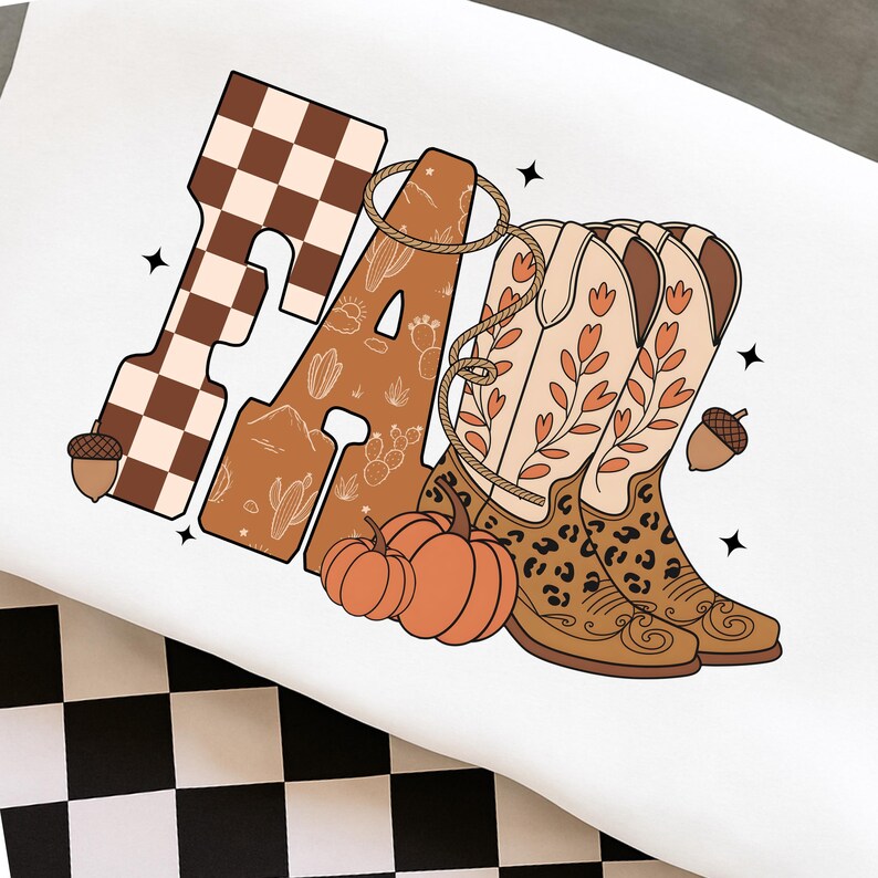 May include: A white t-shirt featuring a graphic design with the word FALL in large letters. The F has a brown and white checkerboard pattern, while the A, L, and L incorporate desert motifs, cowboy boots, pumpkins, and a lasso.