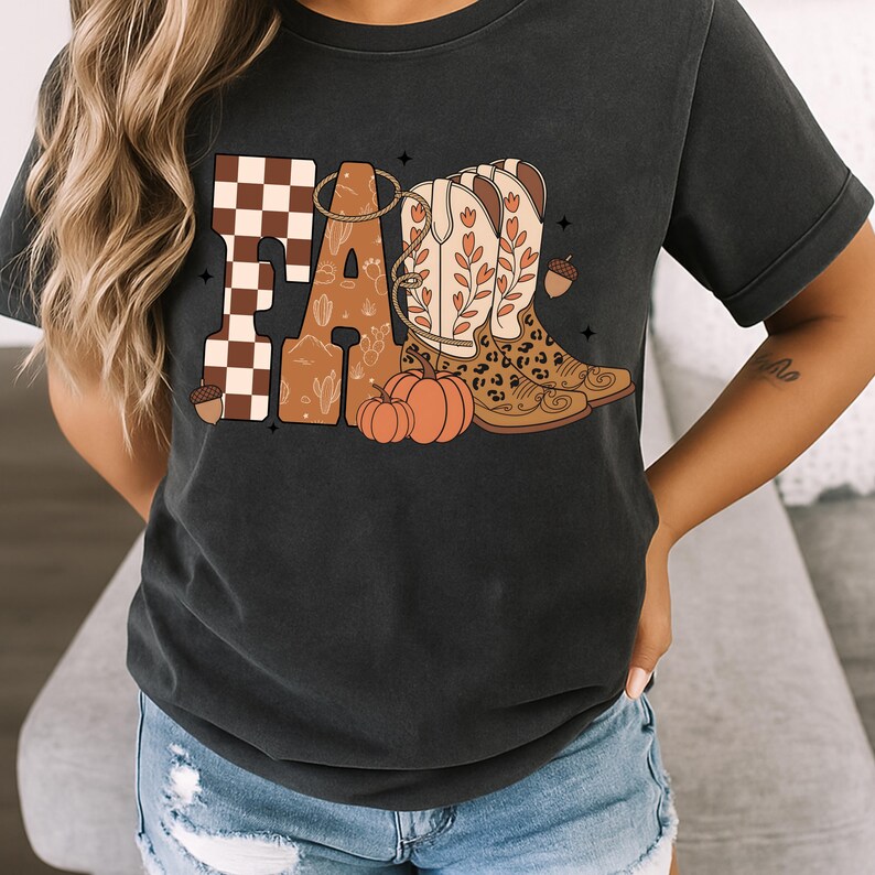 May include: A charcoal gray short-sleeve t-shirt featuring a graphic print that spells FALL. The F is brown and white checkered, the A contains a desert cactus pattern, and the LL are replaced by two cowboy boots with floral and leopard print.