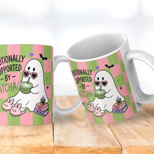 May include: A white ceramic mug featuring a pink and green checkered pattern. The design shows a white ghost wearing heart-shaped sunglasses and bunny slippers, holding a green matcha drink. Text reads: EMOTIONALLY SUPPORTED BY MATCHA.