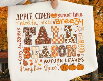 Può includere: Un cuscino bianco a tema autunnale con le parole "FALL SEASON" in vari modelli e colori. Il testo aggiuntivo include "Apple Cider", "Pumpkin Spice" e "Autumn Leaves". Sono presenti anche zucche e foglie autunnali.