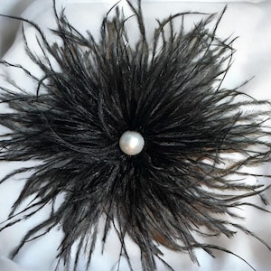 Puede incluir: Una flor de plumas negras con una perla blanca en el centro.