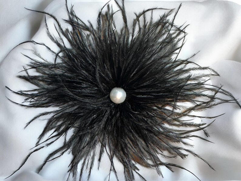 Puede incluir: Una flor de plumas negras con una perla blanca en el centro.
