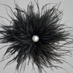 Puede incluir: Una flor de plumas negras con una perla en el centro.
