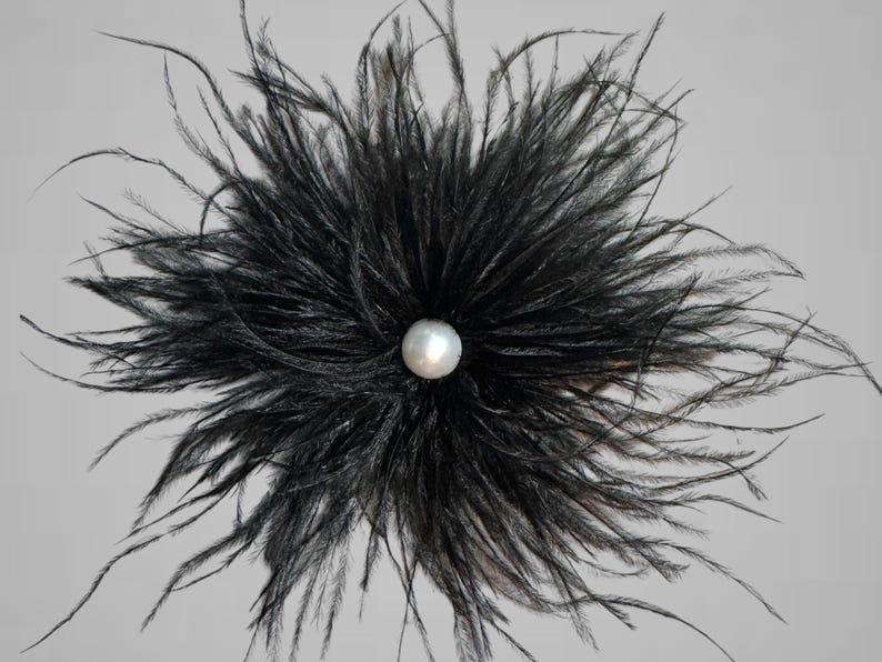 Puede incluir: Una flor de plumas negras con una perla en el centro.