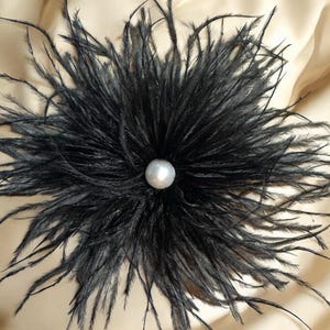 Puede incluir: Una flor de plumas de avestruz negras con una perla en el centro.