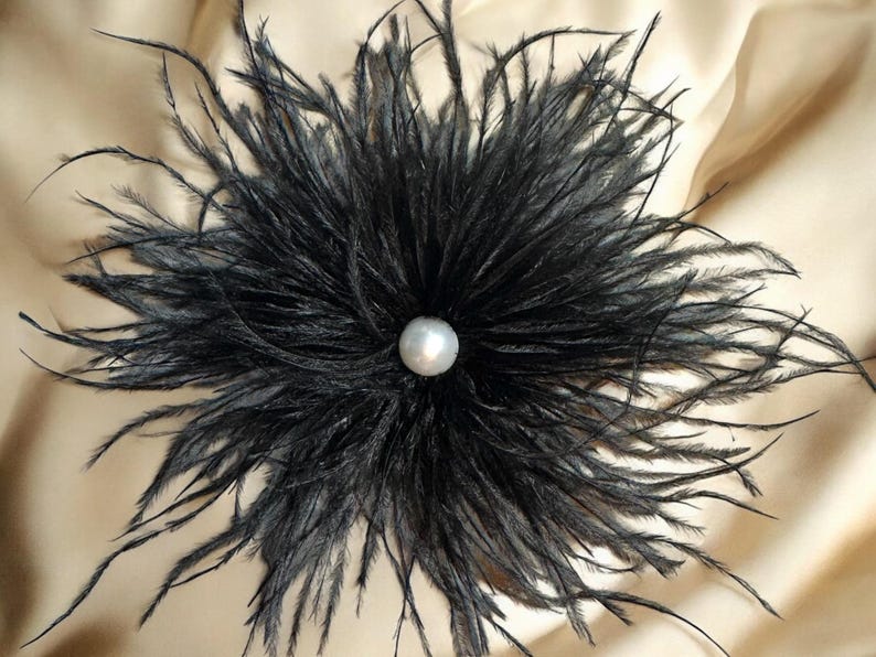 Puede incluir: Una flor de plumas de avestruz negras con una perla en el centro.