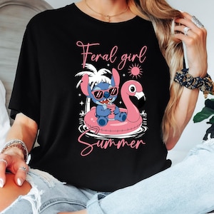 Pu&ograve; includere: T-shirt nera con un personaggio dei cartoni animati con occhiali da sole, che galleggia su un galleggiante a forma di fenicottero rosa. Il testo "Feral girl Summer" &egrave; scritto in rosa. Il design include un sole, palme e stelle.