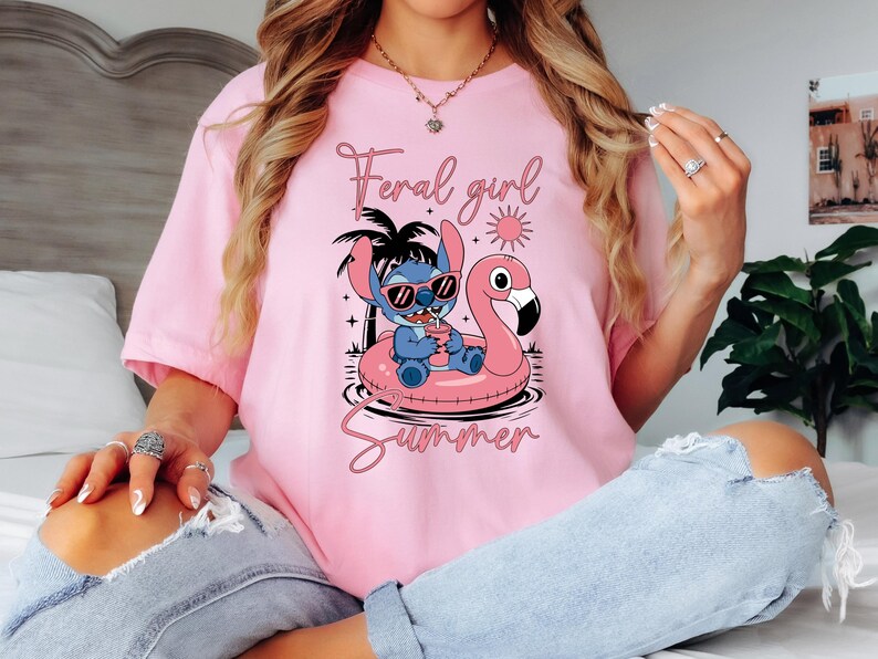 Pu&ograve; includere: T-shirt rosa chiaro con un personaggio dei cartoni animati Stitch con occhiali da sole su un galleggiante a forma di fenicottero rosa. Il testo "Feral girl Summer" &egrave; stampato in corsivo. La maglietta &egrave; a maniche corte.